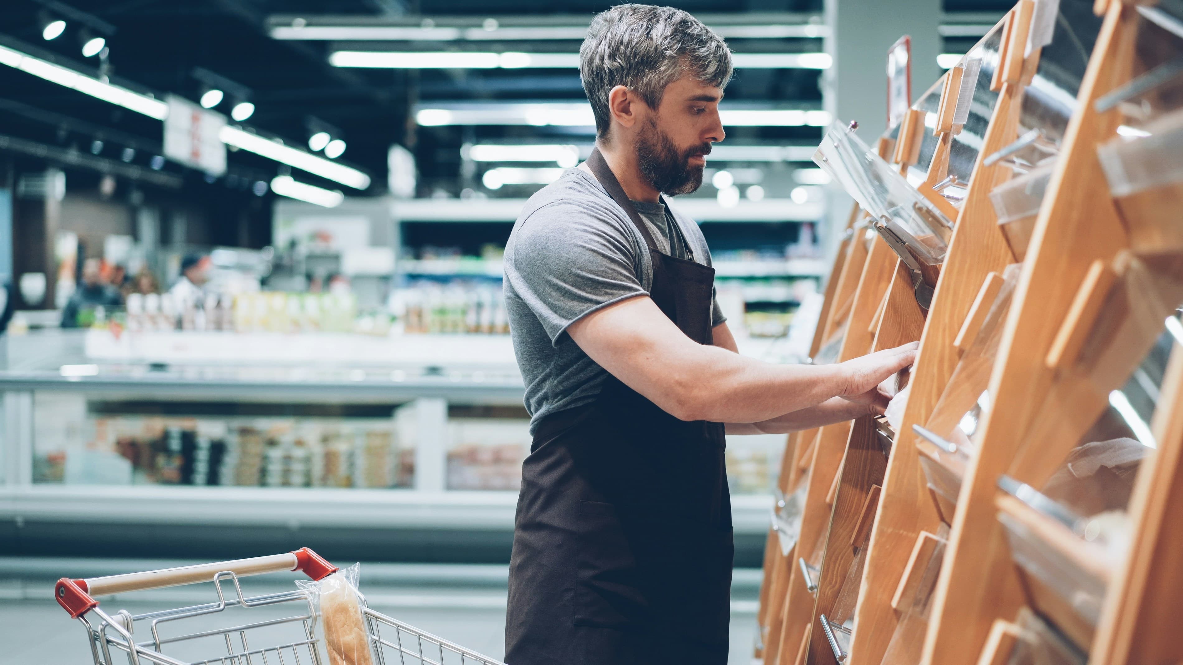 A supermarket worker in an apron restocking bread shelves.